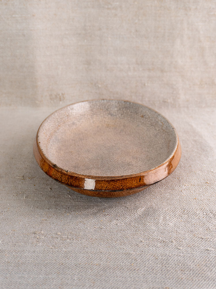 Antique French Provençal Tian with crackle glaze, speckled beige interior, glossy brown rim on textured neutral fabric.