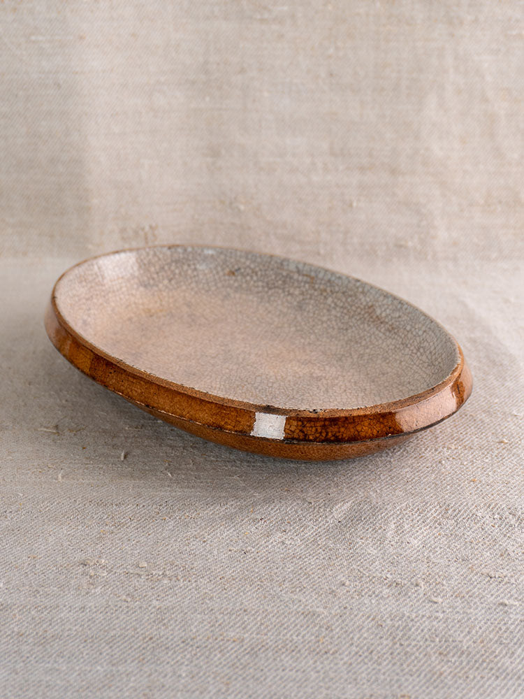 Antique French oval gratin dish with crackle glaze, brown and gray mottled finish on neutral textured fabric.