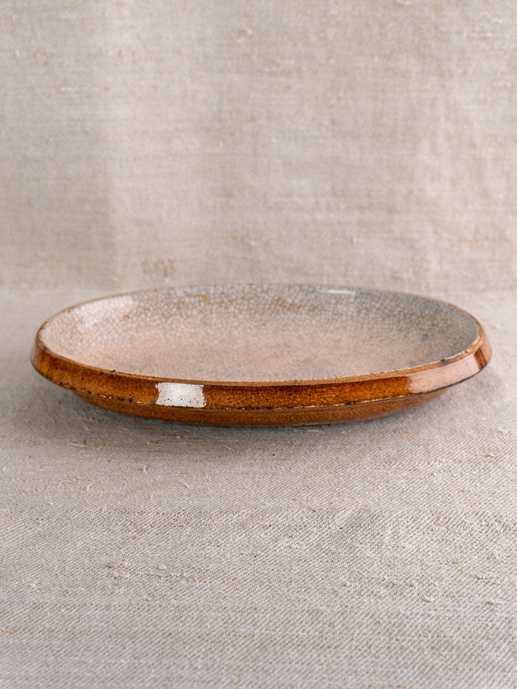 Antique French gratin dish with crackle glaze and brown rim on a neutral textured fabric background.