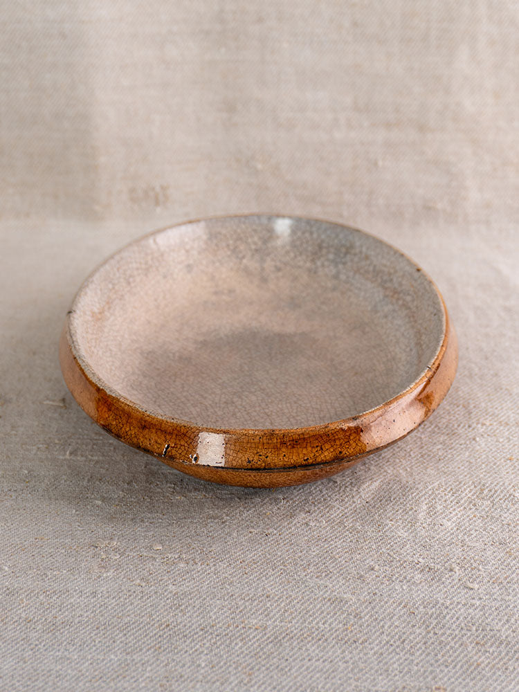 Antique French gratin dish with speckled gray crackle glaze and glossy brown rim, on beige textured fabric.