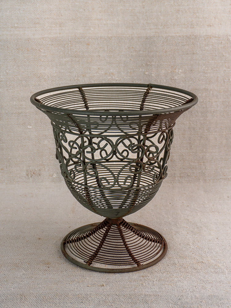 Antique French wire fruit bowl with ornate swirling design and flared footed base on neutral surface.