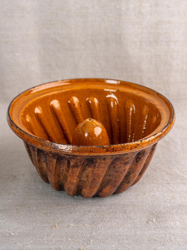 Pair of antique French ceramic Kouglof molds with brown glaze and fluted sides on neutral fabric.
