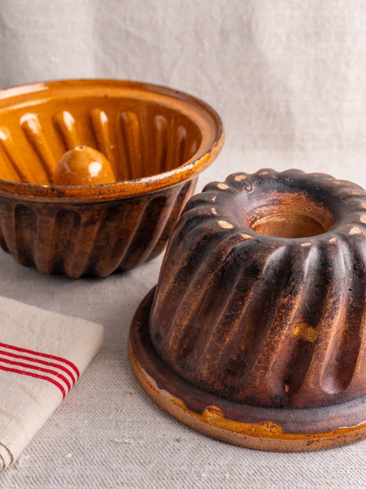 Pair of antique French ceramic Kouglof molds from Alsace on textured beige fabric.