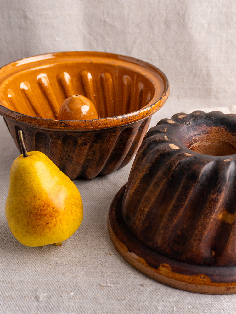 Pair of antique French glazed ceramic Kouglof molds from Alsace, displayed with a yellow pear.