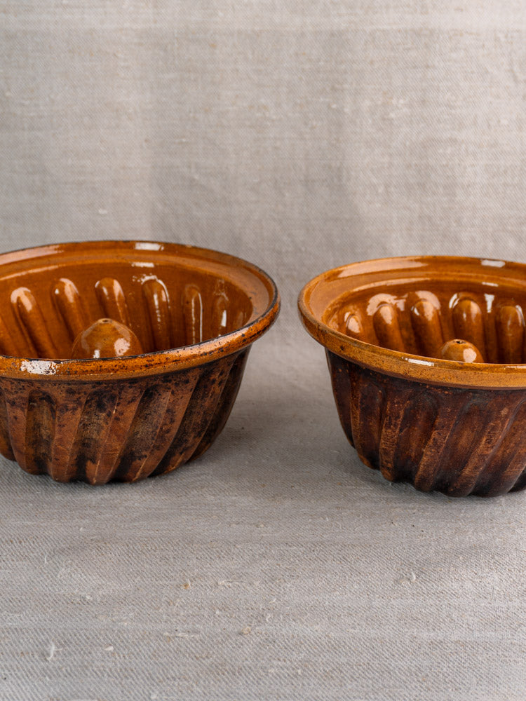 Pair of antique French ceramic Kouglof molds from Alsace on textured beige fabric.
