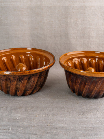 Pair of antique French ceramic Kouglof molds from Alsace on textured beige fabric.