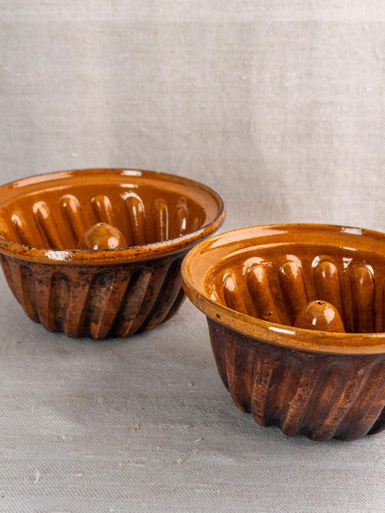 Pair of antique French fluted Kouglof molds in glossy brown glazed Alsace earthenware on beige fabric.