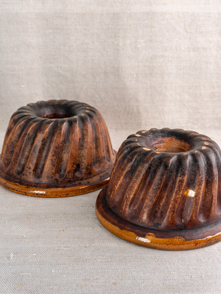 Pair of antique French glazed brown ceramic Kouglof molds reflecting 19th-century Alsace earthenware on beige fabric.