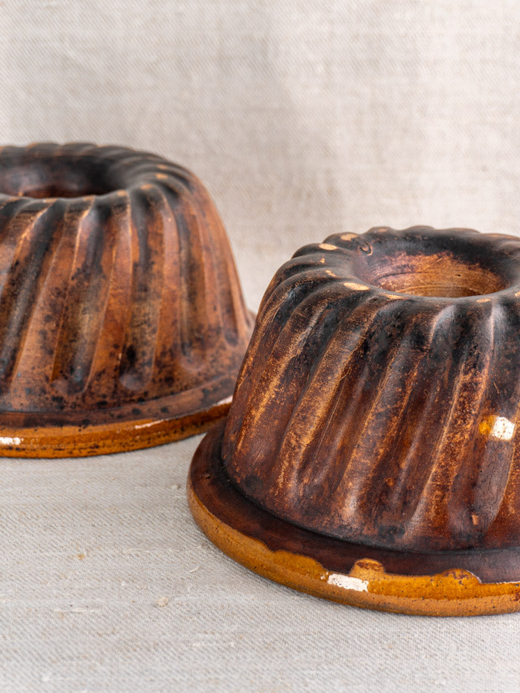 Pair of late 19th-century French Alsace glazed ceramic Kouglof molds on beige textured fabric.