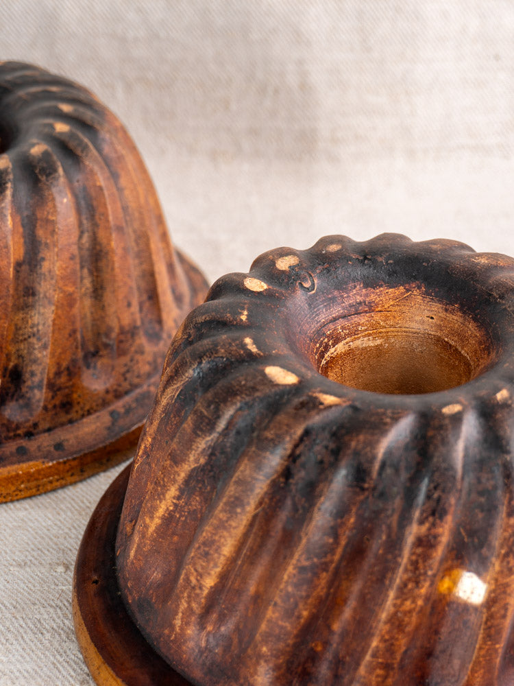 Pair of antique French Kouglof molds with ridged sides and warm brown glaze on fabric.