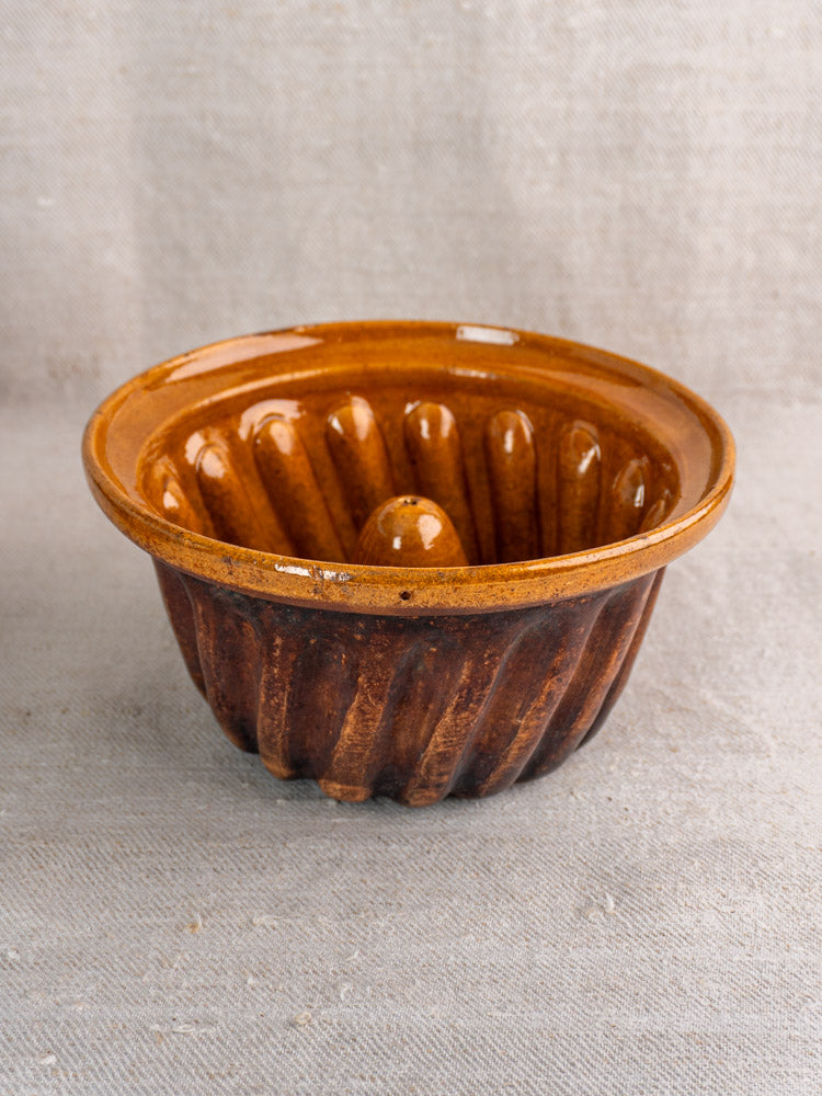 Antique French Kouglof molds pair, brown glazed ceramic with fluted design on light textured fabric.