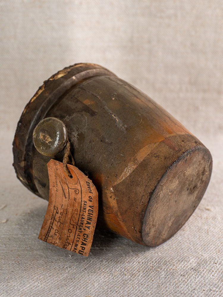 Antique French glazed terracotta Pot à Graisse with original merchant tag on textured fabric with vintage handwritten label.