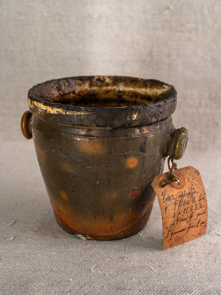 Antique French pot à graisse in dark brown glazed terracotta with two handles and original merchant tag on beige cloth.
