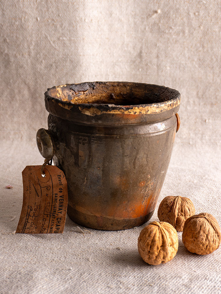 Antique French glazed terracotta pot à graisse with original tag on neutral cloth, next to three walnuts.