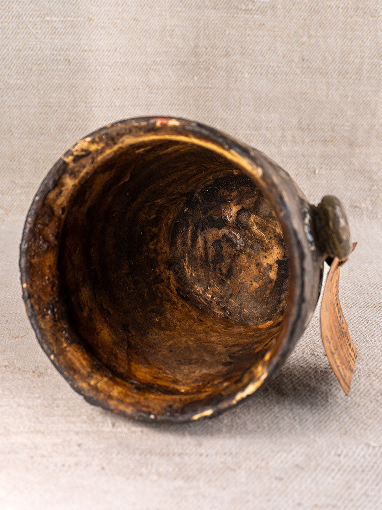Antique French Pot à Graisse in brown glazed terracotta, weathered interior visible, merchant tag attached on textured beige surface.