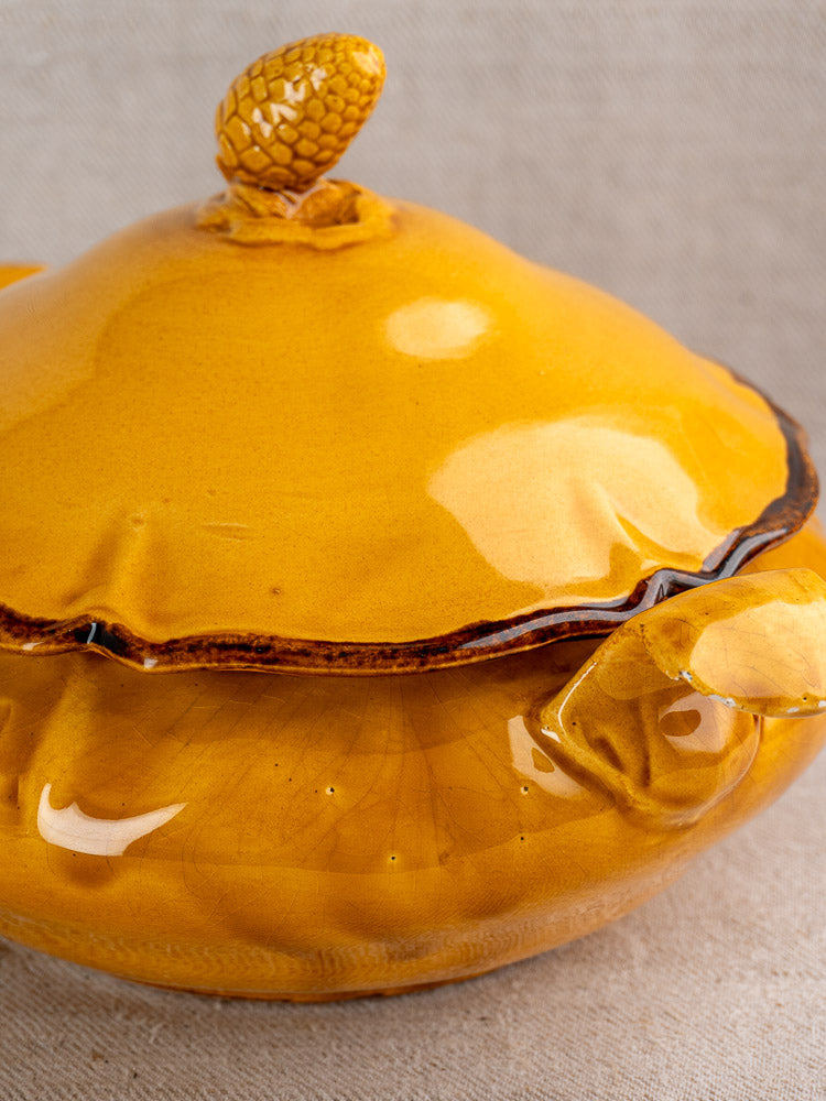 Yellow French faience tureen with pine cone finial, ochre glaze, on neutral fabric background.