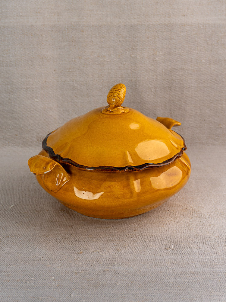 Vintage French Haute Provence yellow faience tureen with pine cone finial, on neutral fabric background.
