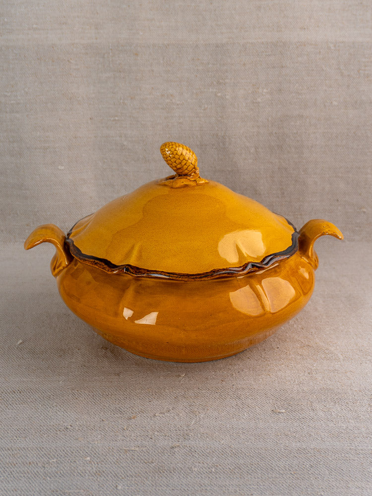 Vintage French Haute Provence yellow faience tureen with double handles and pine cone finial on neutral fabric.