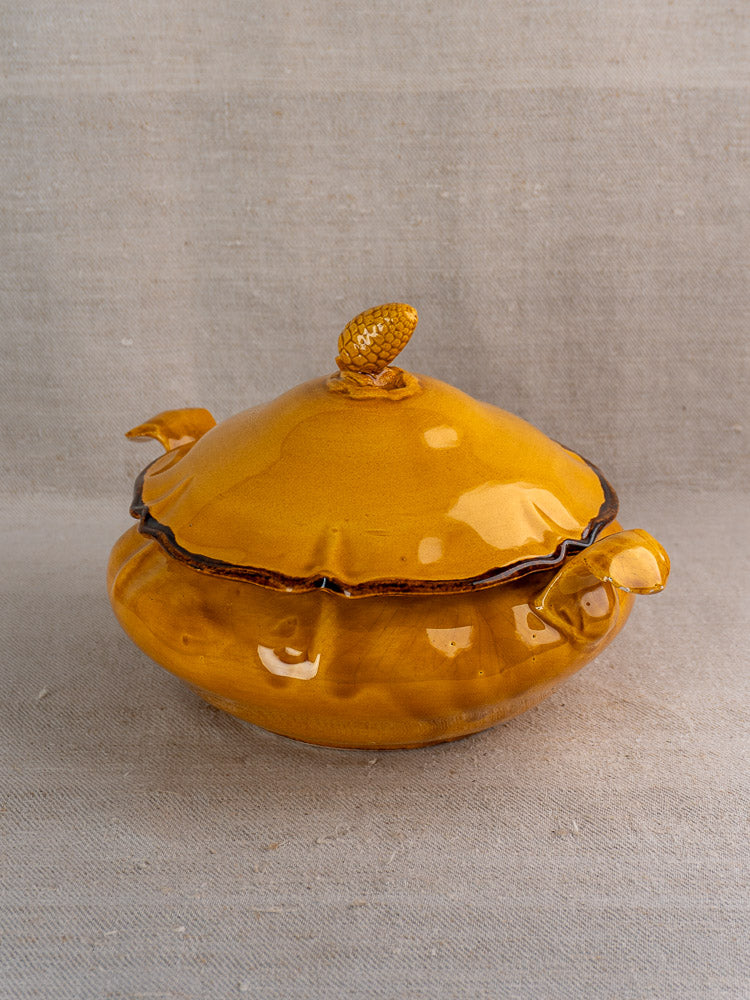 Yellow French Haute Provence faience tureen with ochre glaze and pine cone finial on neutral fabric.