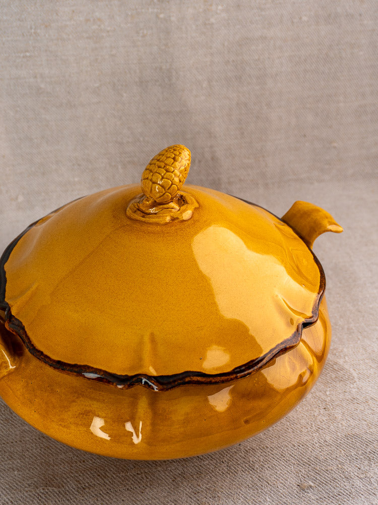 Vintage French Haute Provence yellow faience tureen with pine cone finial on beige fabric surface.