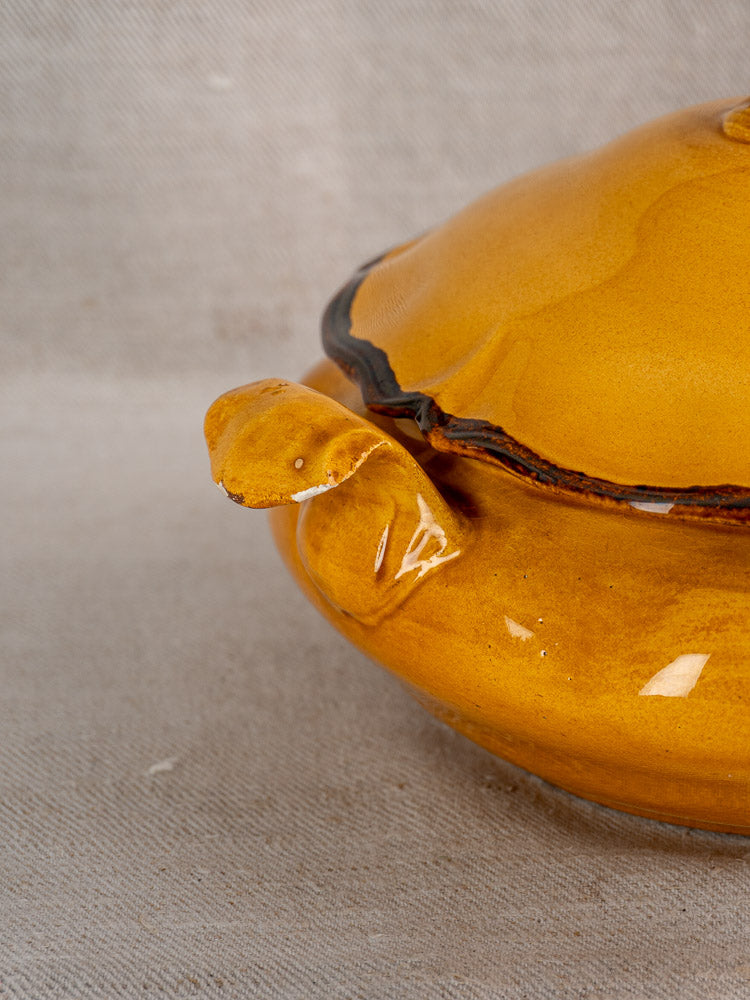 Vintage French Haute Provence yellow faience tureen with brownish-yellow glaze and pine cone finial on beige fabric.