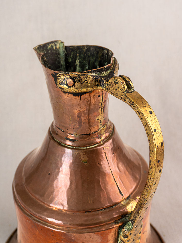 Antique French copper water jug with brass handle, weathered spout, and tarnished patina on a neutral background.