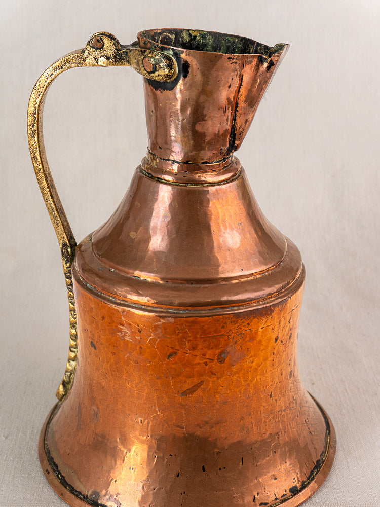 Antique French copper water jug with brass handle, 19th century broc à eau on neutral fabric background.