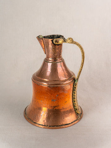 Antique French copper water jug with brass handle, wide base, and narrow neck on a light beige background.