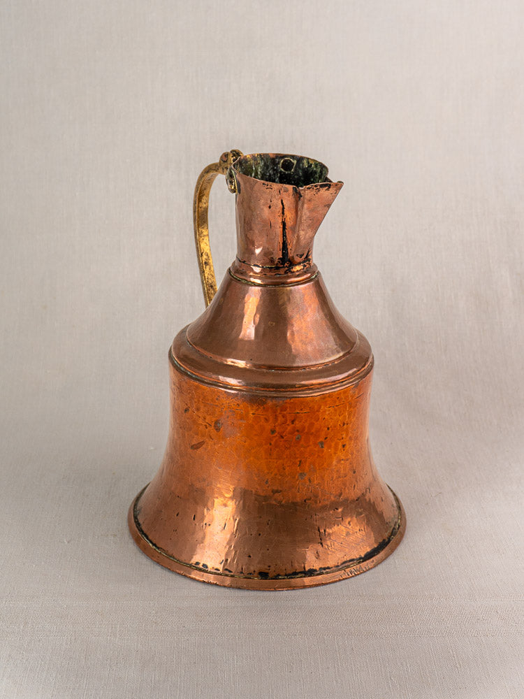 Antique French copper water jug with hammered finish and brass handle, wide base, and narrow neck on a light background.