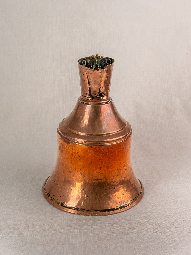 Antique French copper water jug with brass handle, flared base, and tarnished patina stands on neutral fabric.