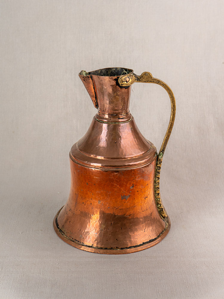 Antique French copper water jug with curved brass handle and hammered finish, wide base, narrow neck, light background.