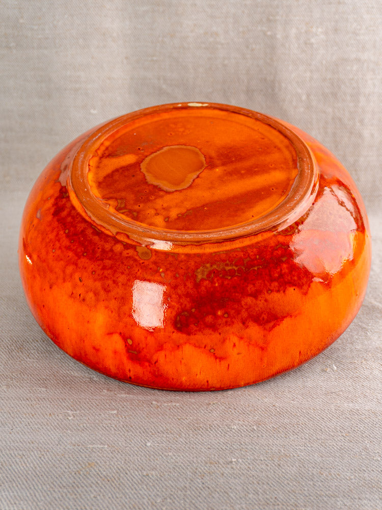 Antique French earthenware serving bowl with vibrant orange glaze, displayed upside down on light gray textured fabric.