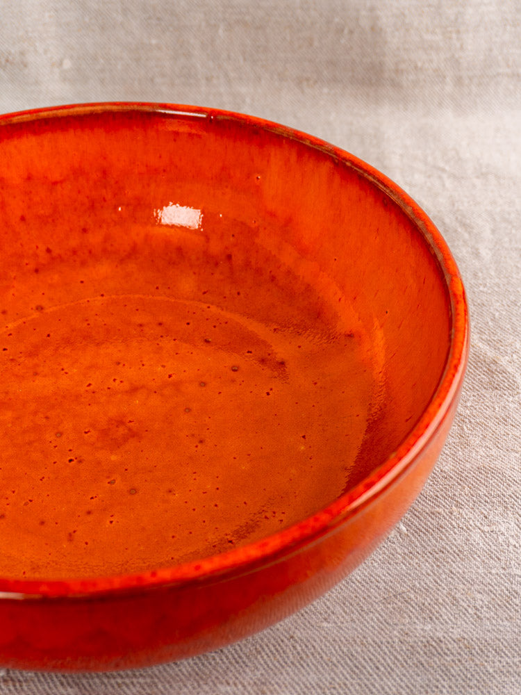 Antique French earthenware serving bowl with vibrant orange glaze, mid-20th century, on light textured fabric.