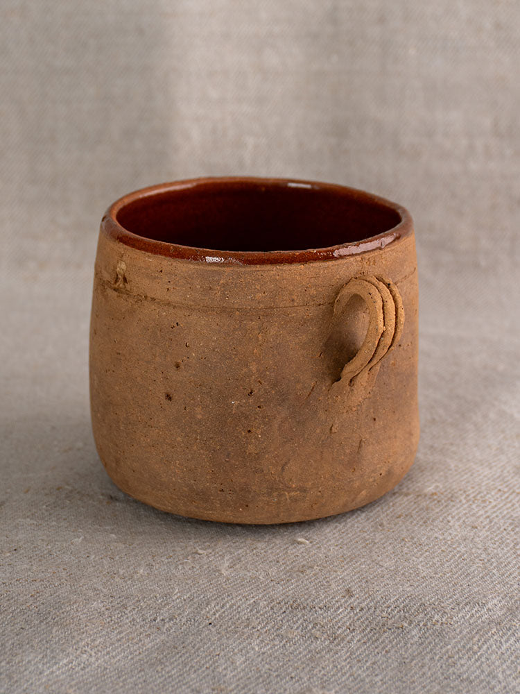 Late 19th century French confit pot with rustic brown glaze and side loop on textured gray fabric.