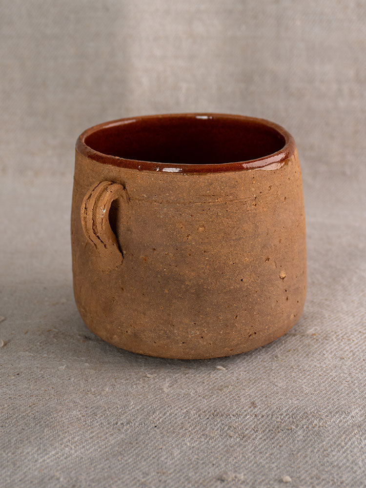 Late 19th century French confit pot with rustic clay body, matte finish, brown glazed interior, on grey fabric.
