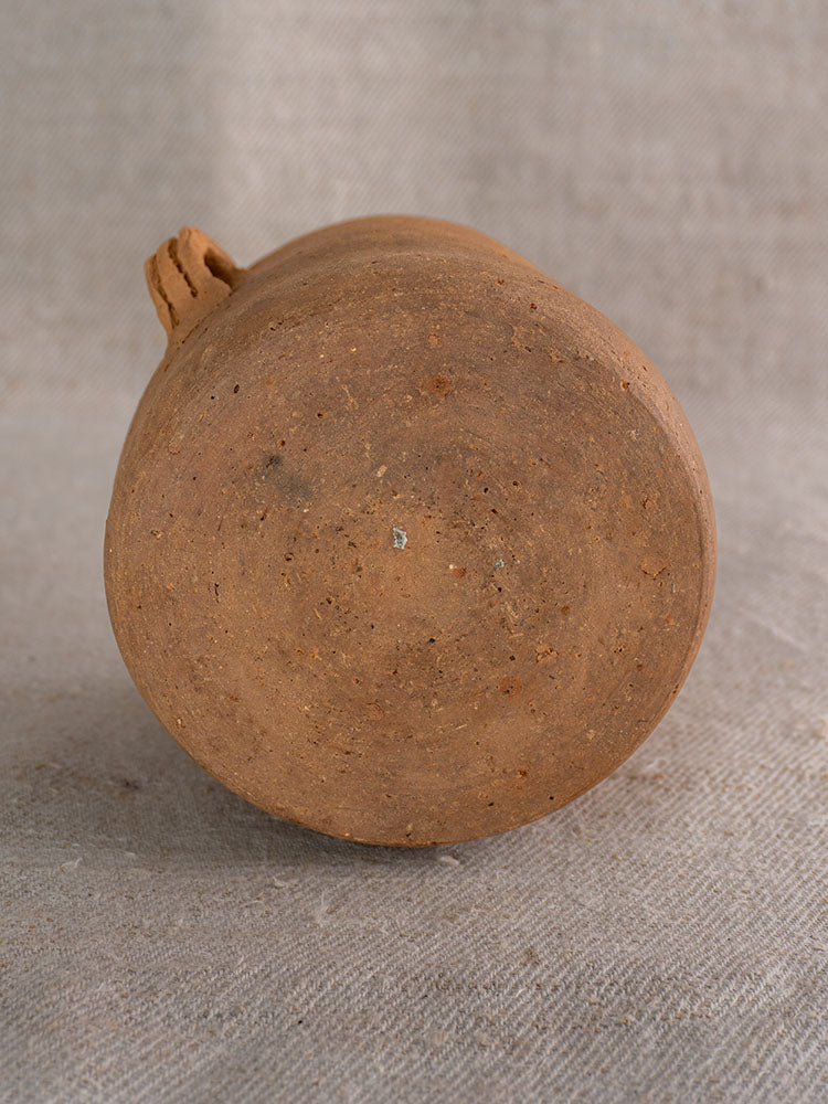 Late 19th-century French confit pot with brown glazed interior, reddish-brown body, on beige fabric.