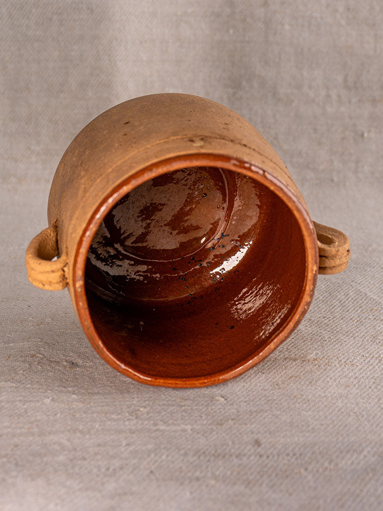 Late 19th-century French confit pot with glossy brown interior, matte exterior, and side handles on gray fabric.