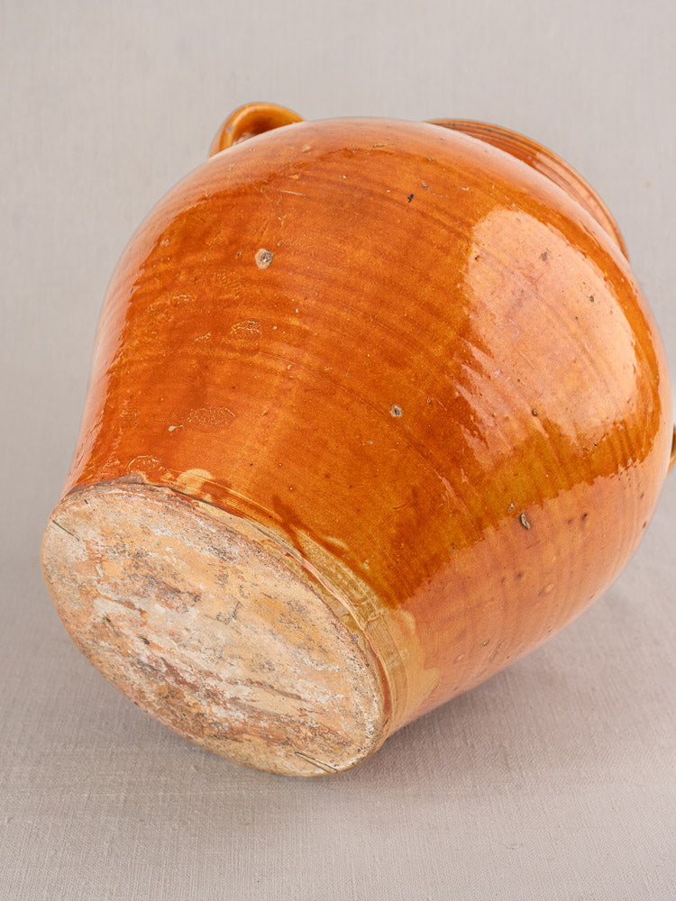 Antique French cruche, late 19th–early 20th century, honey-brown glazed earthenware with rough unglazed base on gray backdrop.