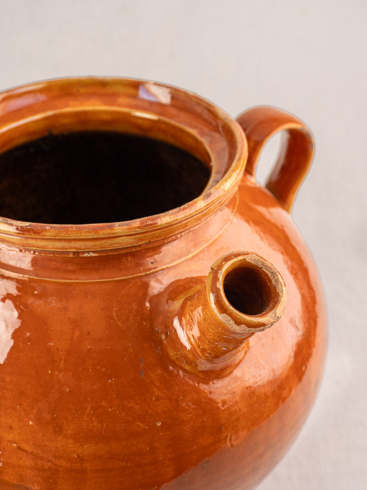 Antique French cruche glazed earthenware water jug with honey-brown finish, round body, side handle, and short spout.