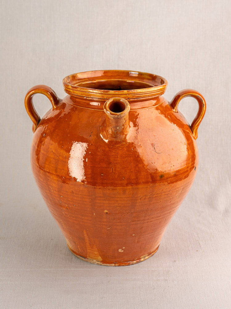 Antique French glazed earthenware cruche water jug with side handles on a light surface, neutral background.