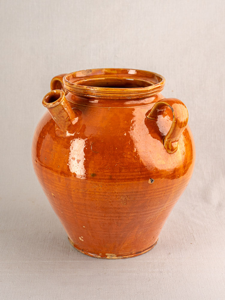 Antique French cruche, honey-brown glazed earthenware jug with two handles and short spout on neutral background.