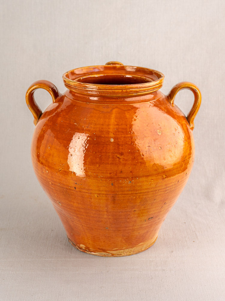 Antique French cruche, late 19th–early 20th century, glazed earthenware with honey-brown finish and side handles on gray background.