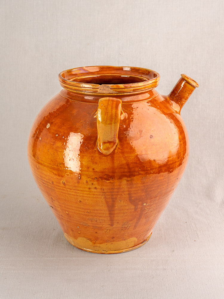 Antique French honey-brown glazed earthenware cruche with two handles and side spout, on a plain light background.