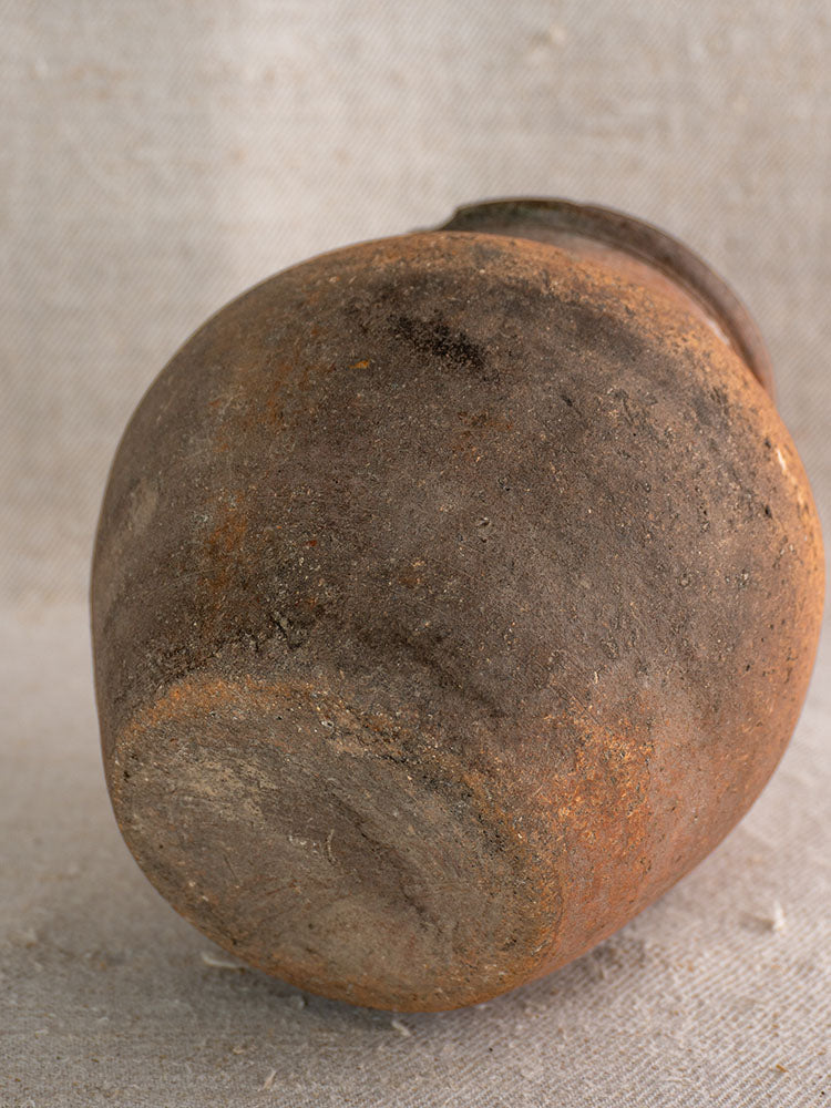 Antique French Toupin Provençal terracotta pitcher with green glaze, weathered surface, on textured beige fabric.