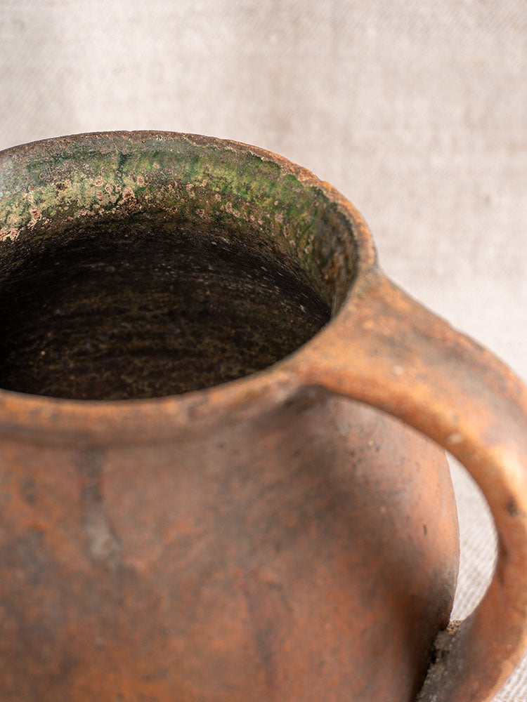 Antique French Provençal terracotta toupin with green-glazed opening and rounded handle, set against a softly blurred background.