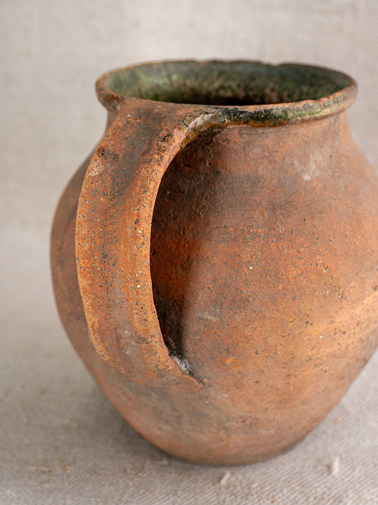 Antique French terracotta toupin with thick handle, orange-brown textured body, green-glazed rim, and aged patina.
