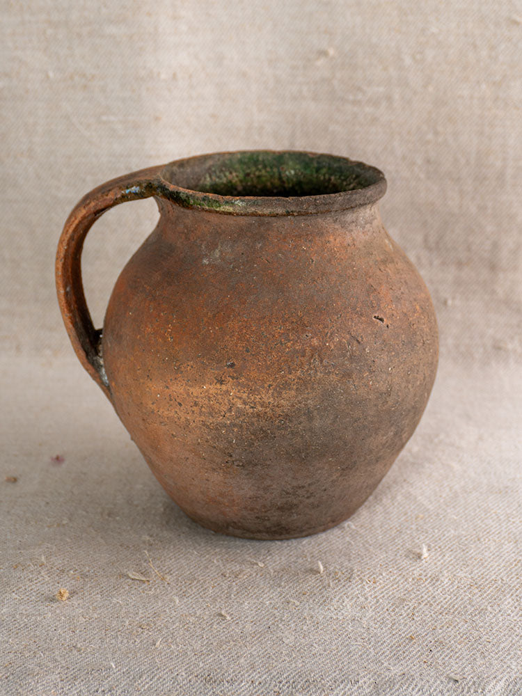 Antique French Toupin Provençal terracotta pitcher with single handle and green-glazed details on beige fabric.