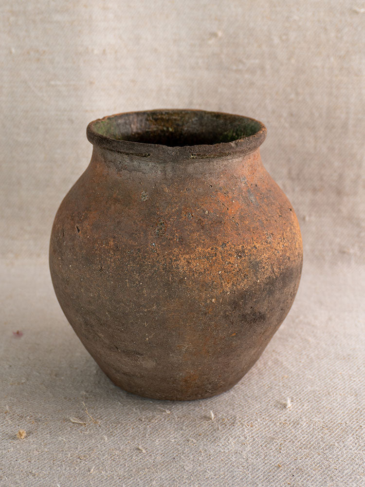 Antique French terracotta toupin with green glaze and weathered finish on textured beige fabric.