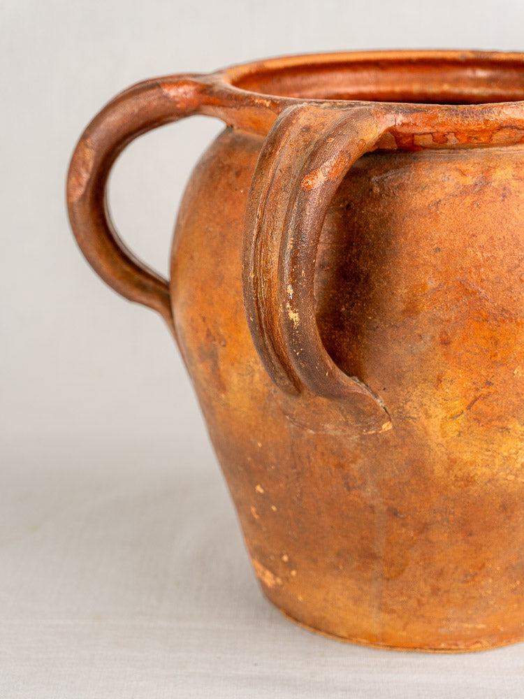 Antique French two-handle glazed earthenware jug with weathered brown surface, Southern France, plain light background.