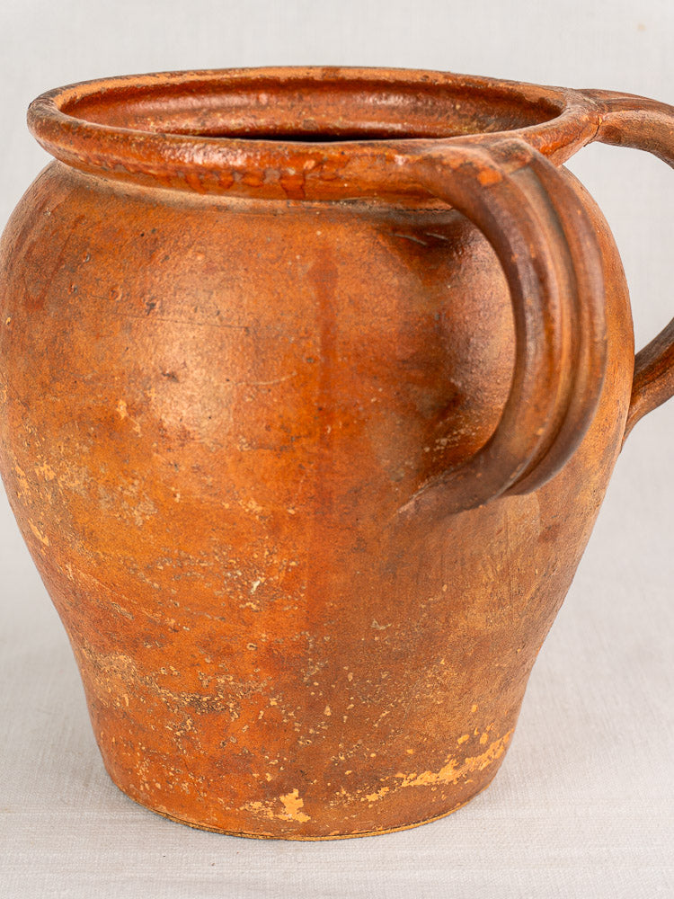 Antique French two-handle glazed earthenware jug from 19th-century Southern France on a light surface. Shows age and wear.